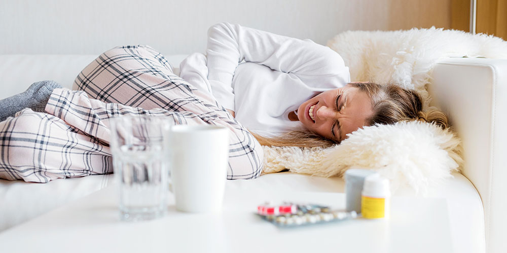 Woman lying on couch in pain, holding abdomen