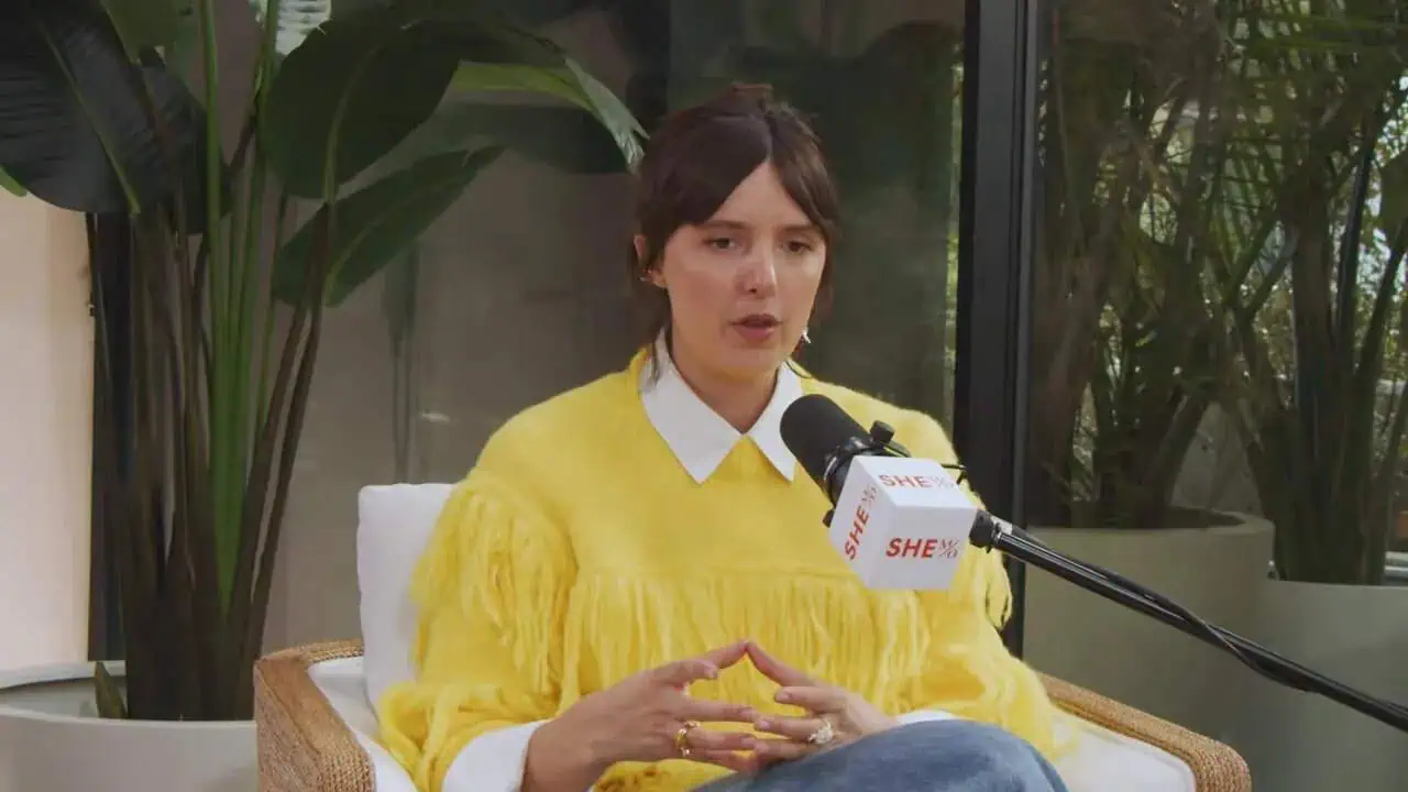 Dr. Thais Aliabadi speaking at a medical event, wearing a yellow outfit and discussing healthcare to.