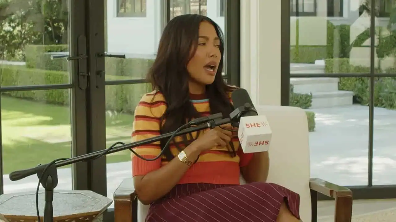 Emma Grede speaking in a podcast interview with microphone and SHE sign in front