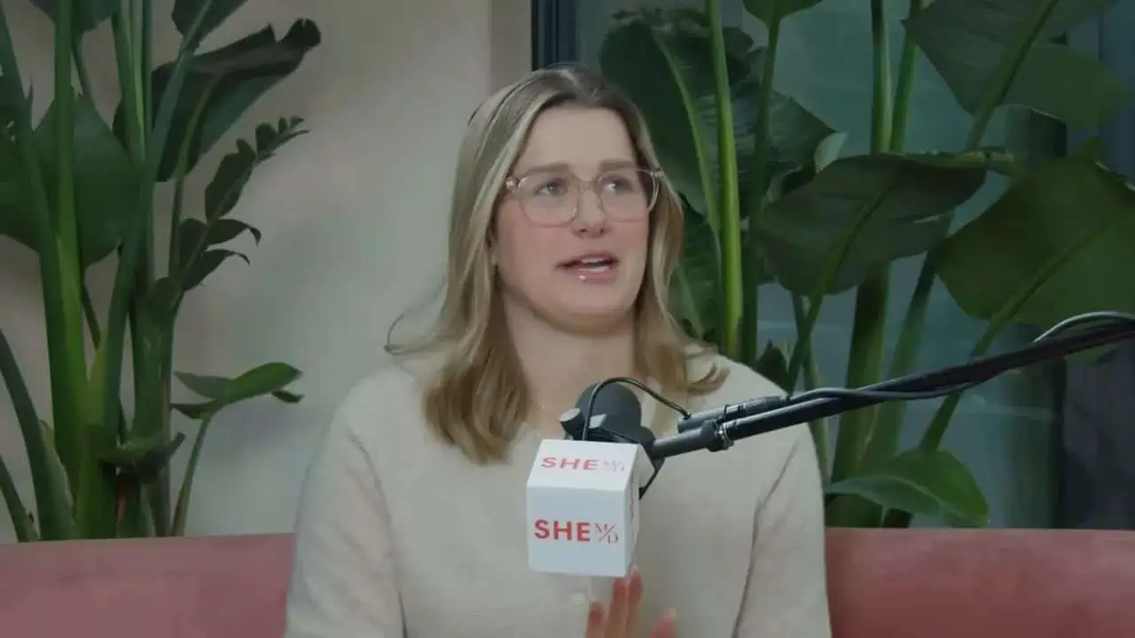 Thais Aliabadi MD speaking at an interview with a microphone in a lush green setting.