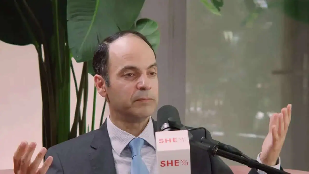 Dr. Ali Abadi speaking at an event, wearing a suit and tie.
