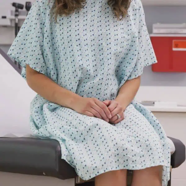 Female patient in hospital gown sitting on examination table.