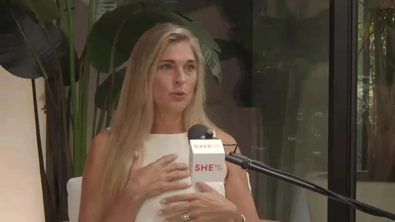 Dr. Thais Aliabadi speaking at a medical event with microphone and plants in background.