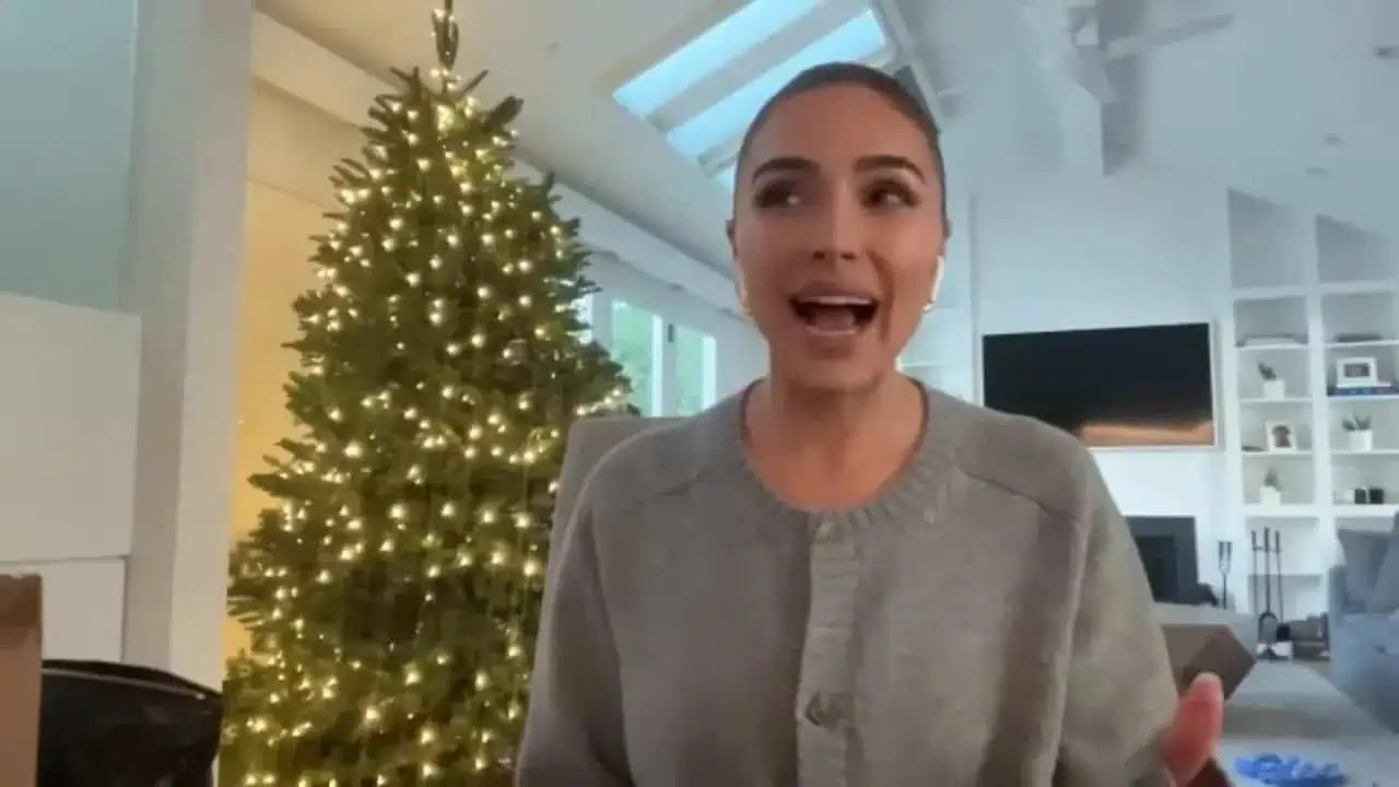 Olivia Culpo speaking with hands raised in front of a Christmas tree