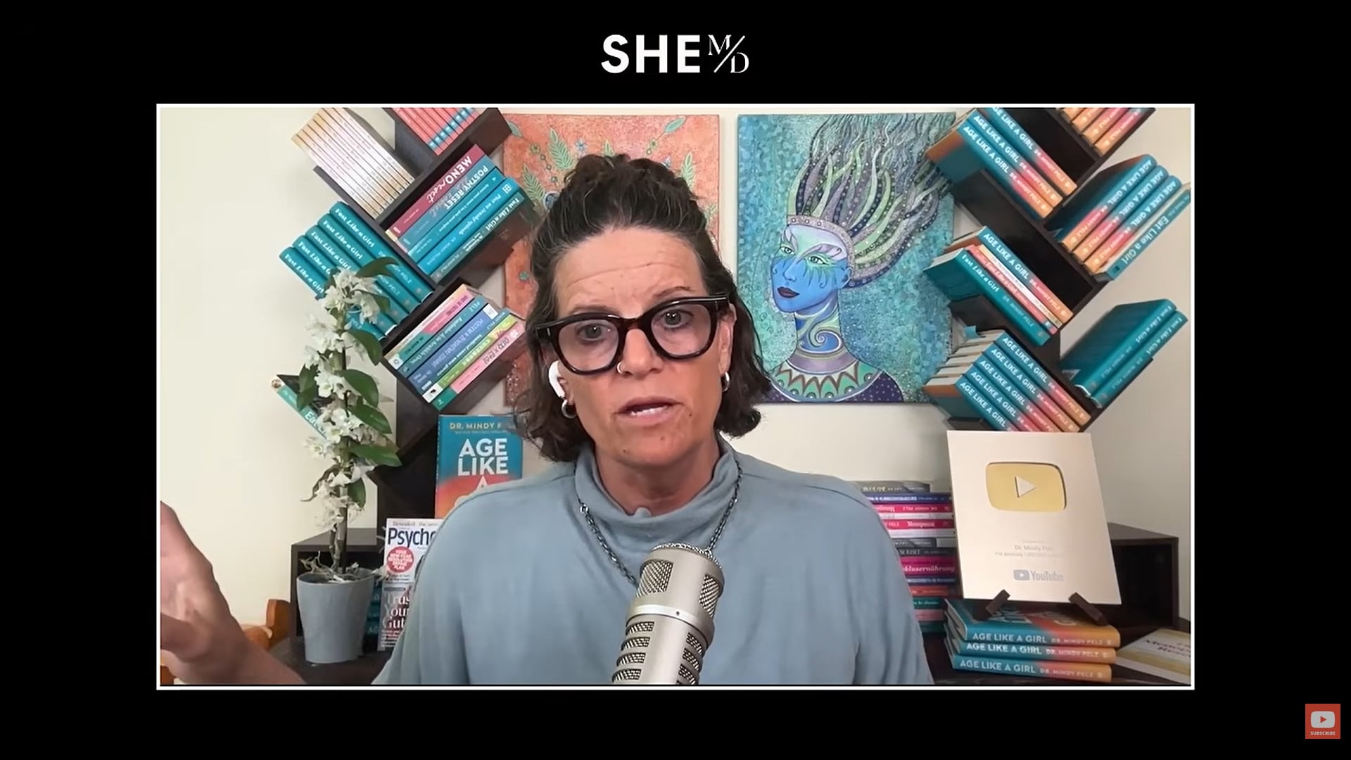 THAIS ALIABADI MD speaking with microphone in a bookshelf studio.